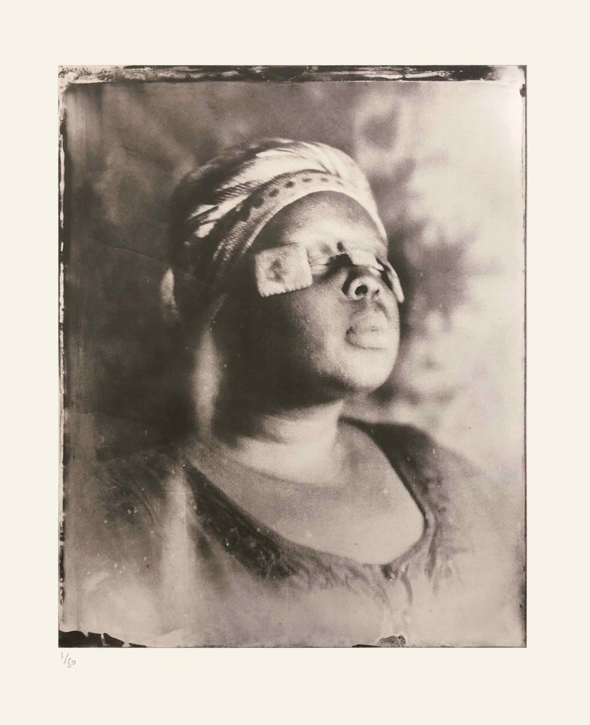 Alt-text: Khadija Saye with three small light-coloured squares, strung together, across her closed eyes