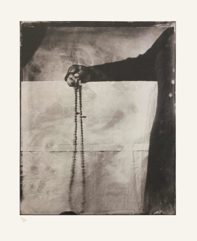 Alt-text: Khadija Saye, only her arm and the side of her body visible, holds a long string of beads