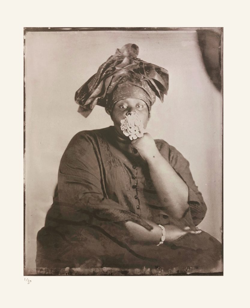 Alt-text: Khadija Saye, facing the camera, holds a large bunch of cowrie shells in her mouth