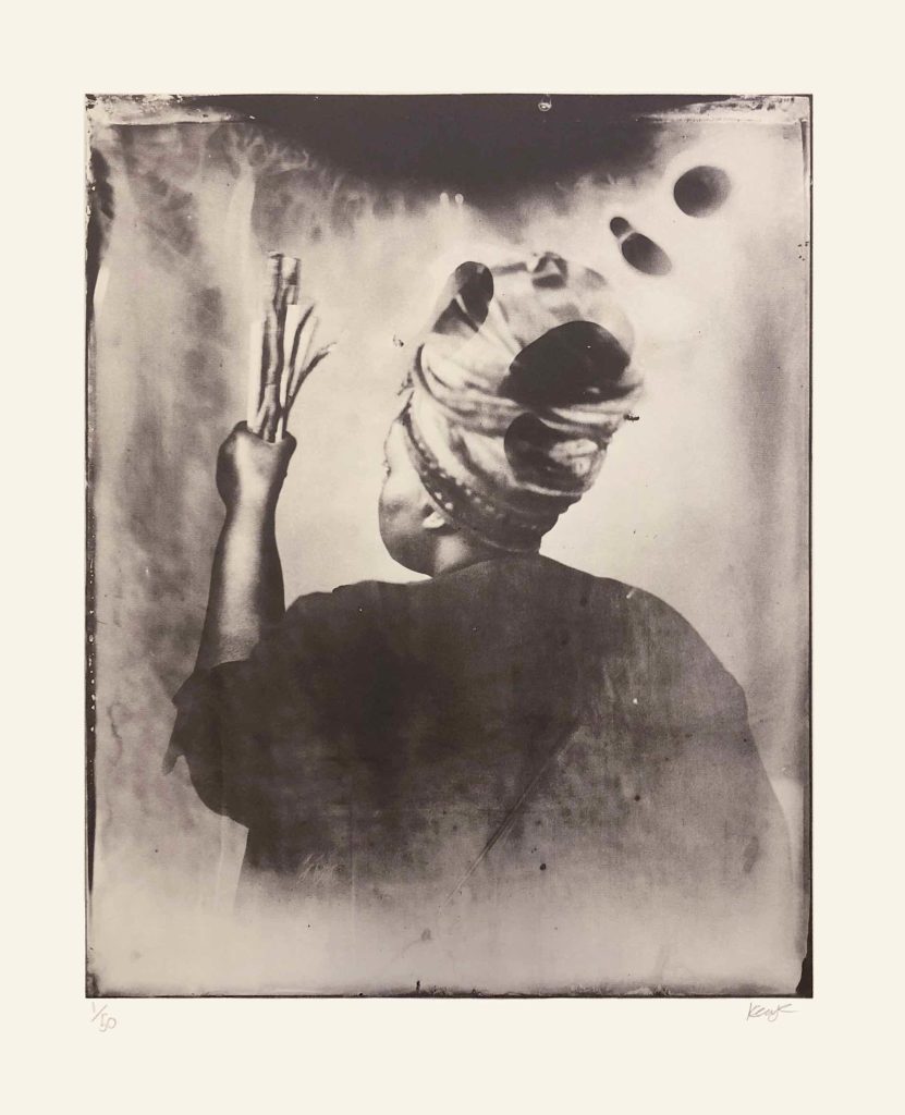 Alt-text: Khadija Saye, her back to the camera, regards different-sized sticks in her left hand